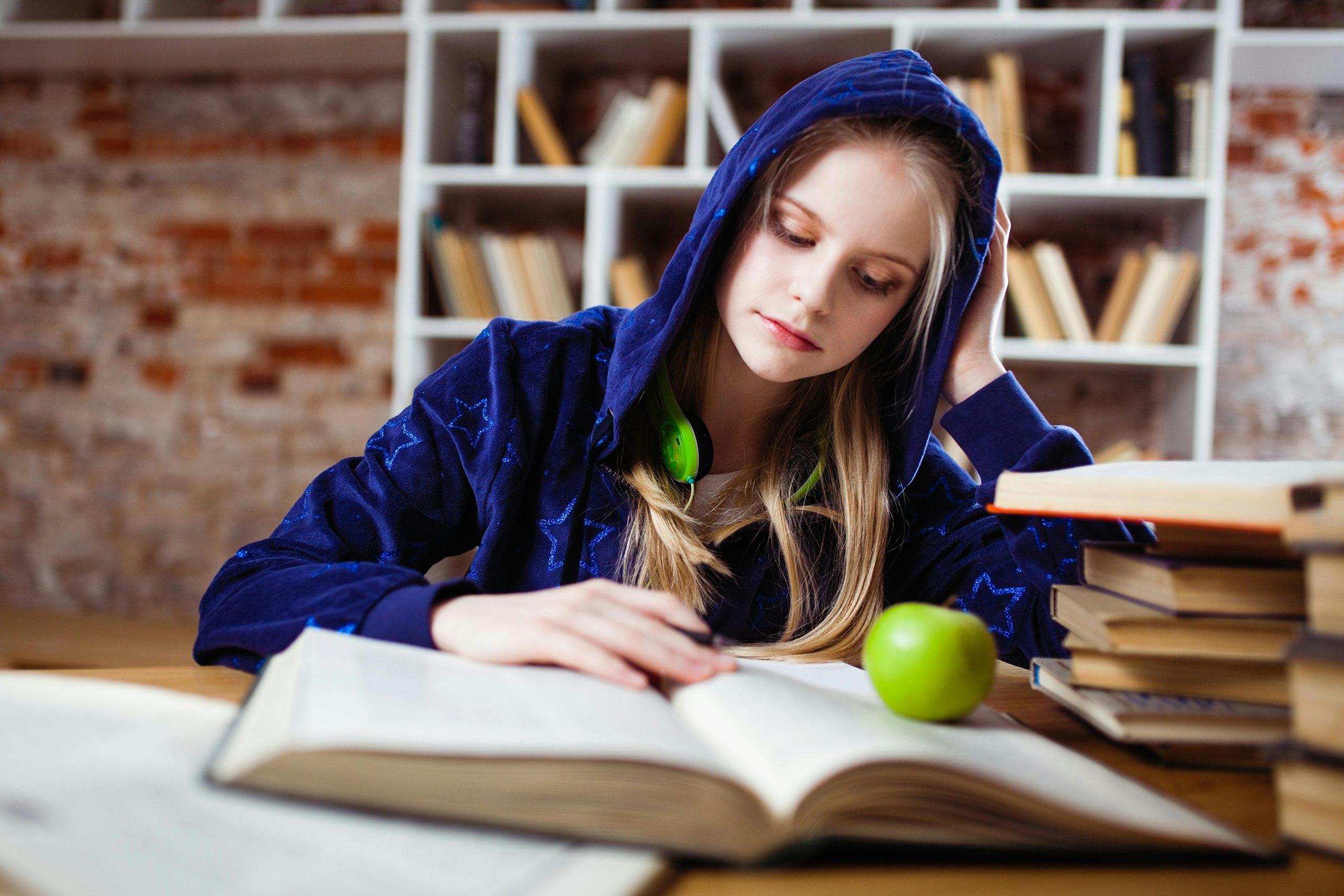 Student reading at a desk with an apple and a stack of books